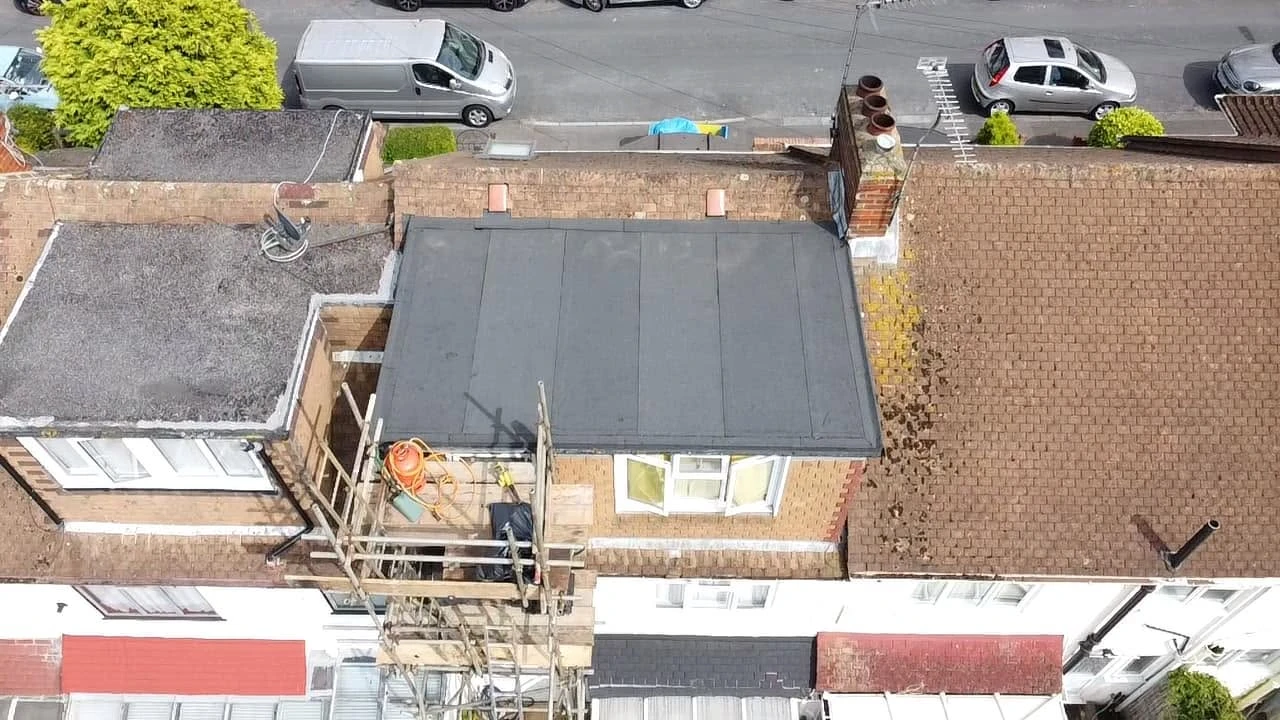 Aerial view of a row of brick houses with one house having scaffolding and construction materials on its flat roof extension under repair.