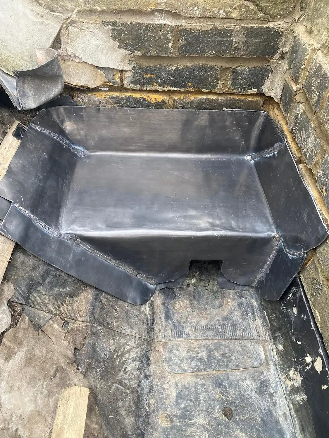 Black waterproof material shaped and fitted against a brick corner wall and floor, appearing to act as a protective liner or barrier.