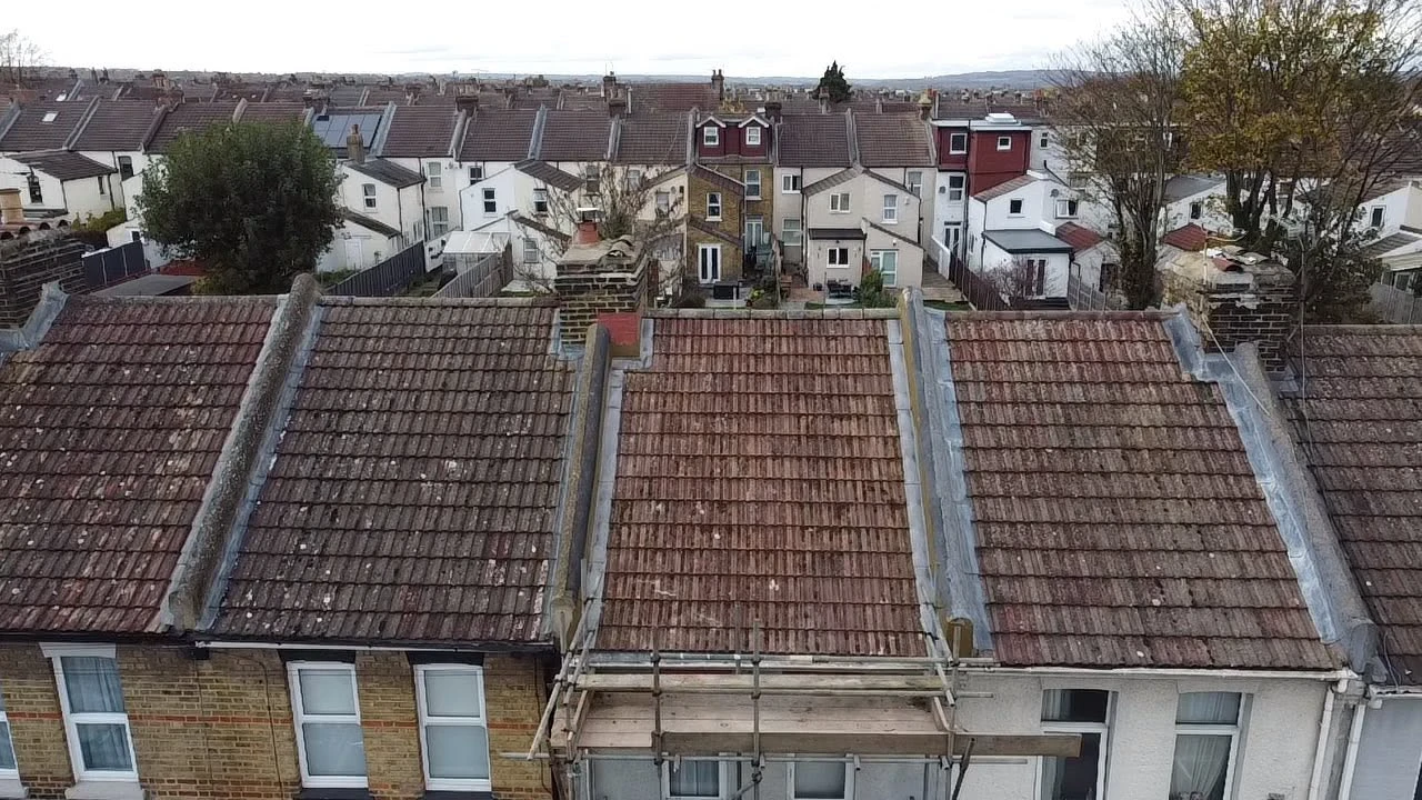 Row of houses with tiled roofs, one roof with scaffolding and chimneys on an overcast day.
